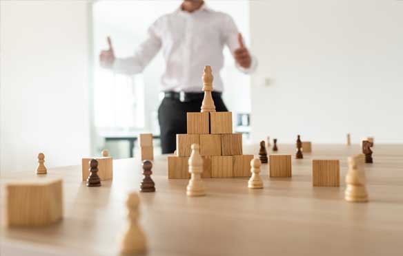 One man showing thumbs up in the background with chess pieces in the foreground. The image represents business consultancy
