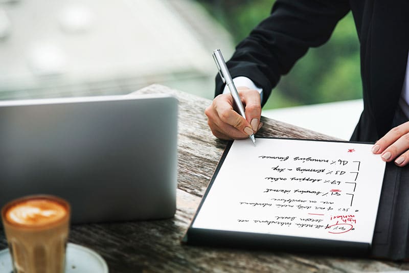 One man writing analysis on a notepad which is kept on a table together with laptop