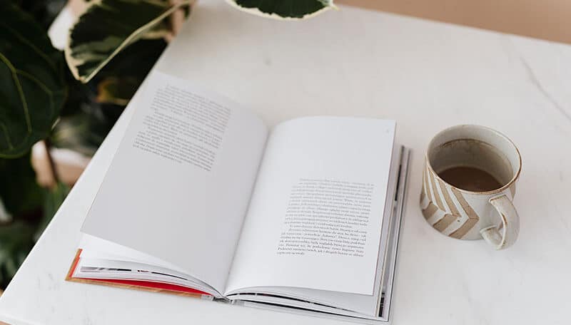 Coffee table book is kept on a table next to a cup of coffee